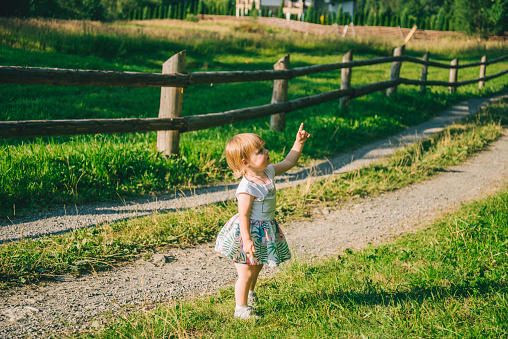 little girl stands on the country raod and point on somtheing, sunny summer day