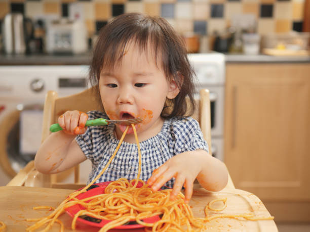 istock baby girl eating messy spaghetti 828872504