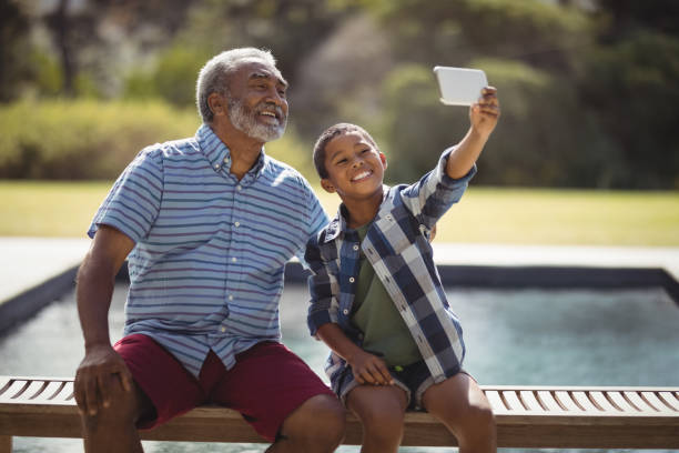 grandson and grandfather taking selfie with mobile phone - swimming pool water people sitting imagens e fotografias de stock