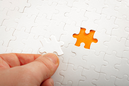 Completing final task, missing jigsaw puzzle pieces and business concept with hand holding the lacking white puzzle piece next to the incomplete or unfinished puzzle on orange background