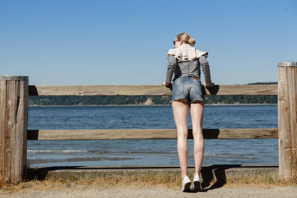 blonde jeune femme en short en jean à la recherche dans le puget sound - se courber en avant photos et images de collection