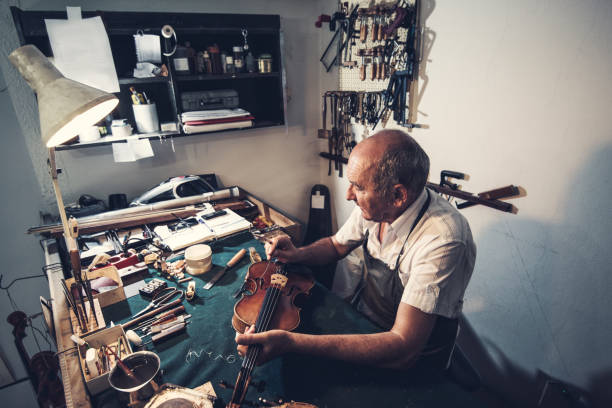vecchio pensieroso che lavora nell'officina di riparazione di strumenti musicali - workshop old fashioned old instrument maker foto e immagini stock