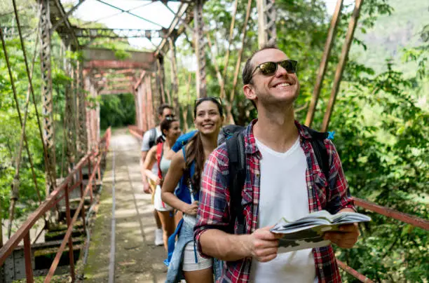 Portrait of a happy man hiking with a group and crossing a bridge - outdoors concepts. Design on map was made from scratch by us.