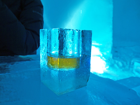 Frozen Shot glass with whiskey made of ice, shaped form frozen water in dark blue ice bar environment