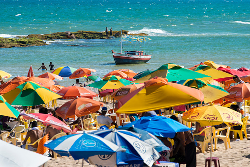 Arembepe, Bahia, Brazil. 04th February 2017. Arembepe beach full of umbrellas on a sunny summer day. Crowded beach and fishing boat floating on the ocean.