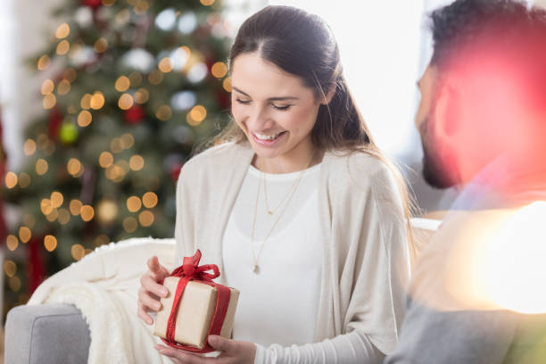 istock Woman enjoys opening Christmas present from her husband 829170176