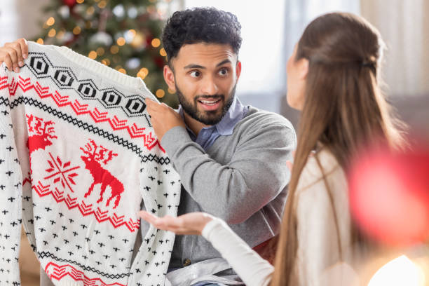 man with funny expression holds up christmas sweater - ugliness sweater kitsch holiday imagens e fotografias de stock