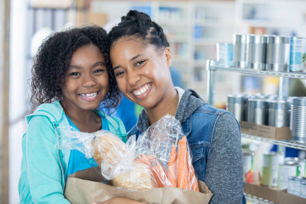 Cute little girl and her mom donate groceries to food bank Adorable elementary age girl and her beautiful mother donate a bag full of groceries to community food bank. food bank stock pictures, royalty-free photos & images