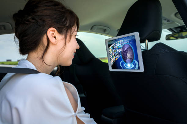 車の後部座席にビデオを見て若い女性。車載インフォテインメントのコンセプトです。 - タクシー ストックフォトと画像