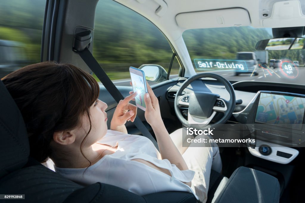 mulher usando telefone inteligente no carro autónomo. autocondução de veículo. piloto automático. tecnologia automotiva. - Foto de stock de Carro sem condutor royalty-free