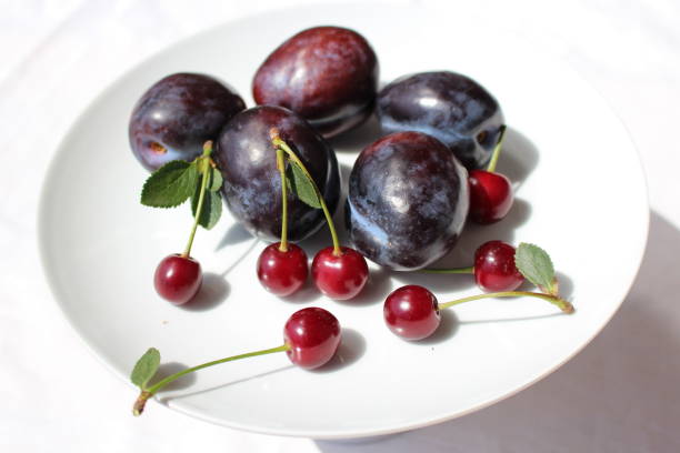 istock Freshly picked organic ripe plums , sour cherries lying on a white plate on a white background 829210932
