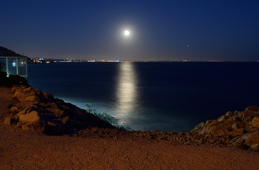 A snapshot of the full moon shining above the city of Santa Monica in the distance, as seen from Malibu down the California coastline.