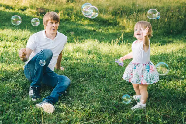 father plays with his daughter with soapbubble outside in the park