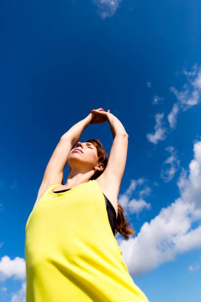 istock Attractive young woman stretching her arms while standing against a deep blue sky, exercising on a sunny day. 829302990