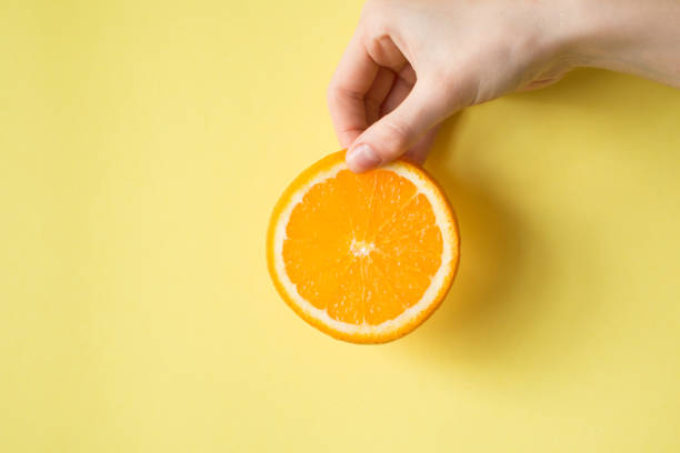 istock Hand holding orange on yellow background food concept 829309938