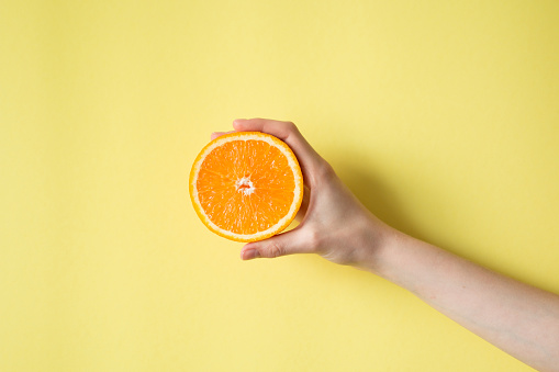 Hand holding orange on yellow background food concept