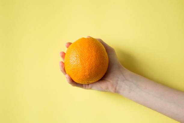 istock Hand holding orange on yellow background food concept 829310390