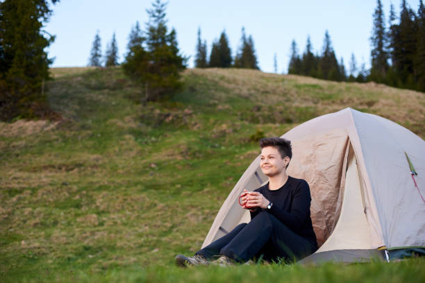 istock Happy female hiker drinking tea in front camp tent. 829363368