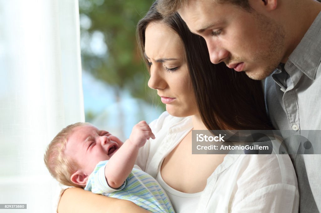 Tired desperate parents and baby crying Tired desperate parents holding their baby crying desperately at home Baby - Human Age Stock Photo