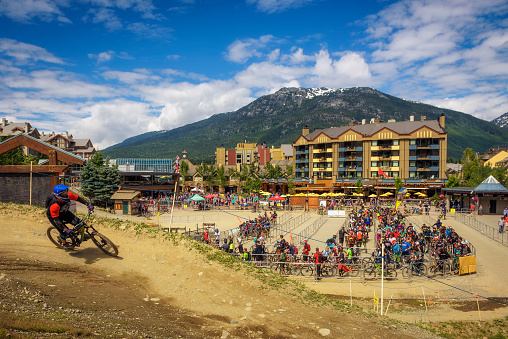 Whistler, British Columbia: Biker riding a mountain bike in the Whistler Mountain Bike Park with many bikers waiting in line in the background.