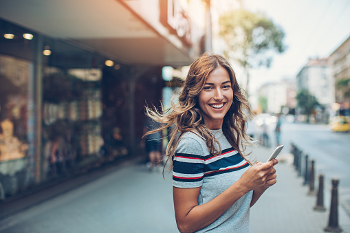 Smiling young woman with smart phone walking on the street