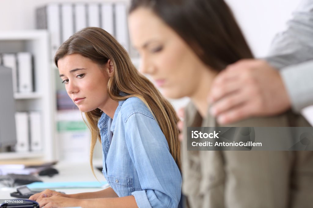 Employee being victim of harassment and colleague watching Disgusted employee being victim of harassment and a colleague watching her Harassment Stock Photo