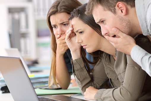 Three worried employees reading bad news on line in a laptop at office
