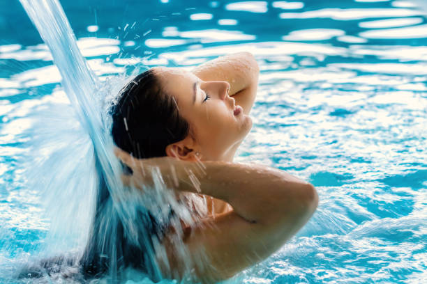 Young woman enjoying water cascade in spa. Close up portrait of young girl with relaxed facial expression under high pressure shower in spa.Woman touching hair with eyes closed. health spa stock pictures, royalty-free photos & images