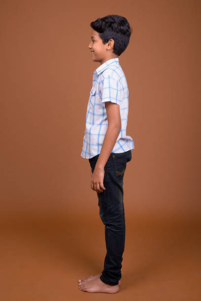 Studio shot of young Indian boy wearing checkered shirt against colored background Studio shot of young Indian boy wearing checkered shirt against colored background vertical shot indian boy barefoot stock pictures, royalty-free photos & images