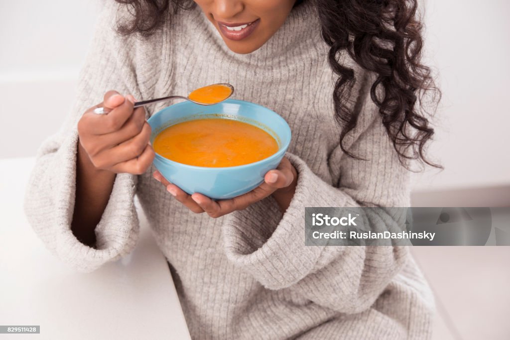 Woman enjoy hot soup at winter. Close up unrecognized hungry woman eating Tom Yum hot Thai soup at winter. Woman wearing winter sweater, sitting at the kitchen table. Soup Stock Photo