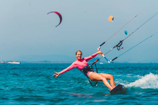 Young female kiteboarder enjoying kiteboarding Young female kiteboarder on the water, active summer holidays by the sea, windy weather, surfing and kiteboarding, adrenaline sports kiteboarding stock pictures, royalty-free photos & images