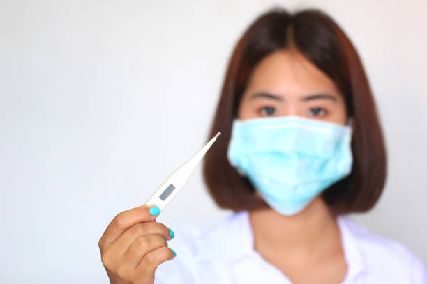 Worried Asian mom measuring her sick daughter's temperature while she rests in bed, ensuring she receives the comfort and attention she needs during a moment of illness