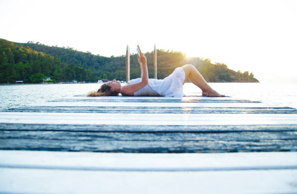 Young woman lying on jetty above lake, reading book