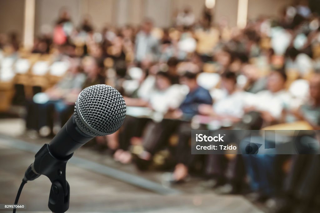 Microphone over the Abstract blurred photo of conference hall or seminar room with attendee background Conference - Event Stock Photo