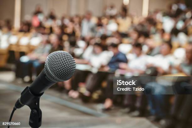 Microphone Over The Abstract Blurred Photo Of Conference Hall Or Seminar Room With Attendee Background Stock Photo - Download Image Now