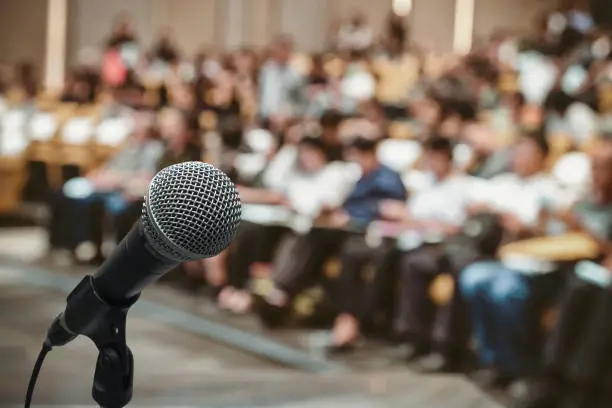 Photo of Microphone over the Abstract blurred photo of conference hall or seminar room with attendee background
