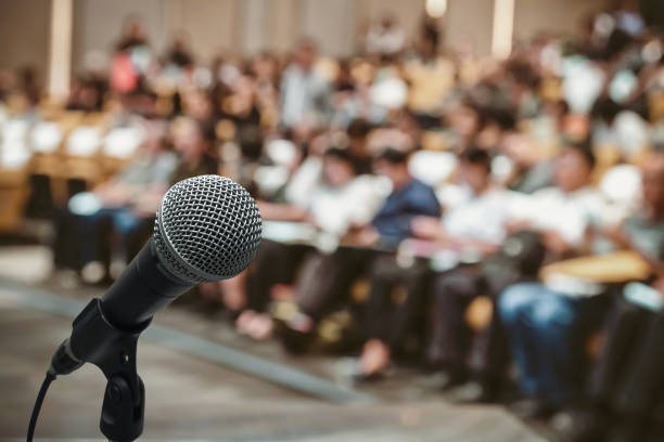 microphone over the abstract blurred photo of conference hall or seminar room with attendee background - audience imagens e fotografias de stock