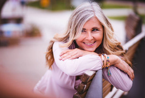 Beautiful smiling mature woman with grey hair and fashionable clothes sitting on a park bench