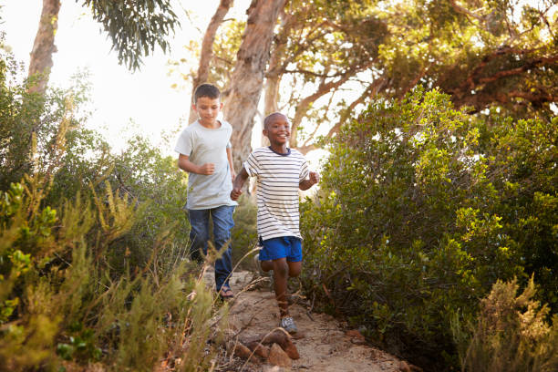 two smiling young boys running down a forest path - healthy lifestyle nature sports shoe childhood imagens e fotografias de stock