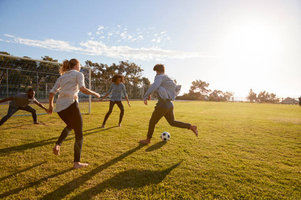 Four young adults playing football in a park at sunset Four young adults playing football in a park at sunset soccer soccer ball kicking adult stock pictures, royalty-free photos & images