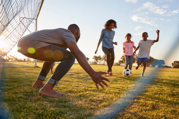 un ragazzo prende a calci un calcio durante una partita con la sua famiglia - termine sportivo foto e immagini stock
