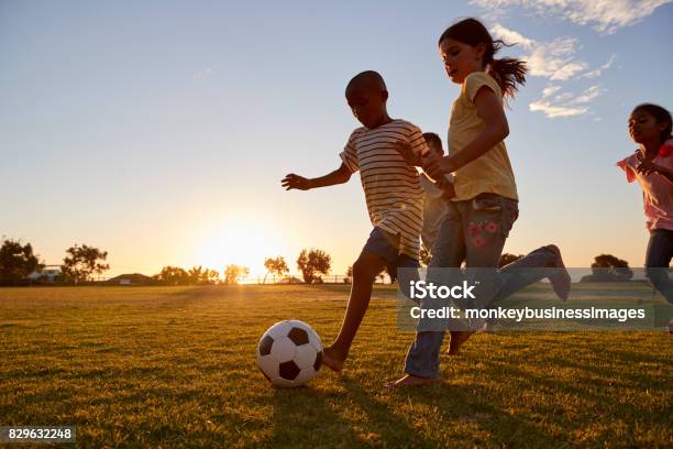 Four Children Racing After A Football Plying On A Field Stock Photo - Download Image Now