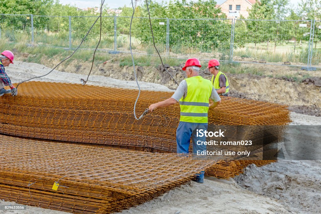 Workers are helping mobile crane to pile up of armature, rusty square reinforcement Zrenjanin, Vojvodina, Serbia – June 29, 2015: Building activities during construction of the large complex shopping mall "AVIV PARK" in Zrenjanin city. Abundance Stock Photo