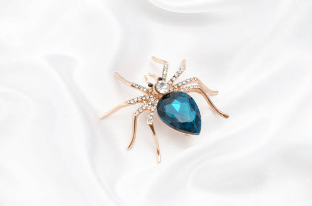 istock Golden spider with a big blue stone on silk fabric 829656074