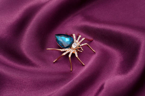 Golden spider with a big blue stone on silk fabric