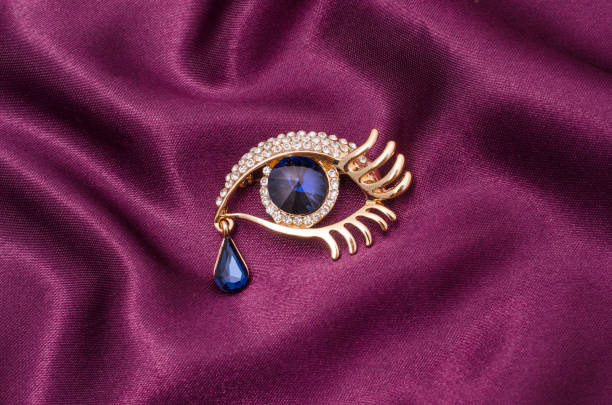 istock Gold brooch eye with diamonds with large sapphire on a silk fabric 829656218