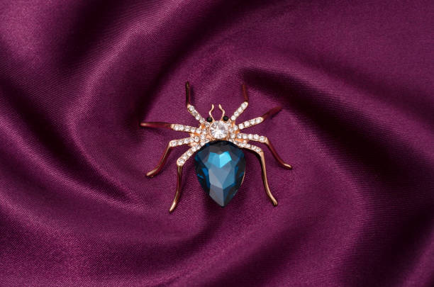 istock Golden spider with a big blue stone on silk fabric 829656220