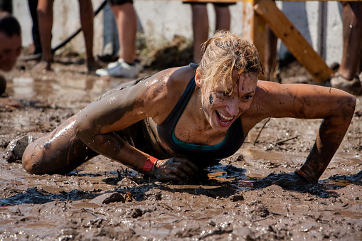 Young woman smiling and crawling under barbed wire; concept of winning, endurance, strength and fun