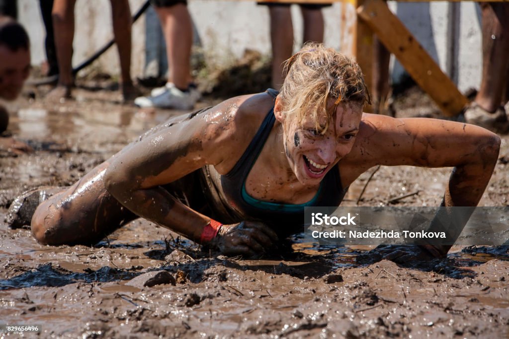 A woman crawling under barbed wire Young woman smiling and crawling under barbed wire; concept of winning, endurance, strength and fun Obstacle Course Stock Photo