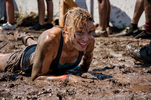 young woman crawling in the mud; participation in extreme sport, physical strength challenge